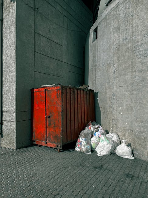 A large accumulation of mixed household waste and rubbish is scattered across a hard surface, likely a driveway or pavement. The debris includes numerous plastic bottles, some with visible labels, crumpled paper and newspaper, and various discarded packaging materials. Several bottles appear to be partially crushed or empty, with different shapes, sizes, and textures, primarily made of transparent or darker plastic. Among the waste, there are also crumpled paper bags, torn cardboard, and other miscellaneous rubbish. The scene appears to be outdoors, with natural lighting casting minimal shadows over the cluttered area. Some waste items are stacked or leaning against each other, creating a chaotic pile typical of fly tipping or improper disposal. This image visually underscores the importance of proper rubbish handling and waste clearance, which companies like Waste Clearance Lewisham provide through private and alternative disposal services, helping to prevent illegal dumping and ensure tidy environments.